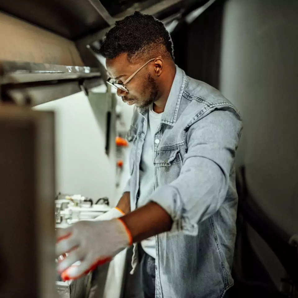 Black engineer in denim work jacket peers into a hood