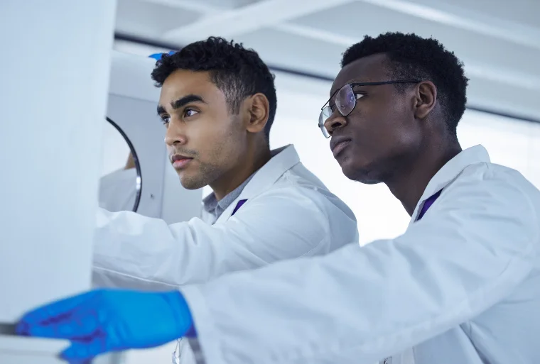 Two men in white lab coats observe an off-camera action