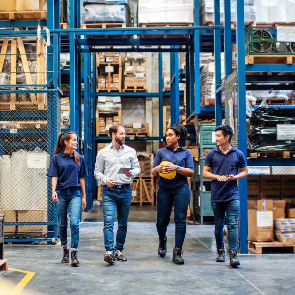 Two men and two women walk across the factory floor towards the camera while deep in conversation